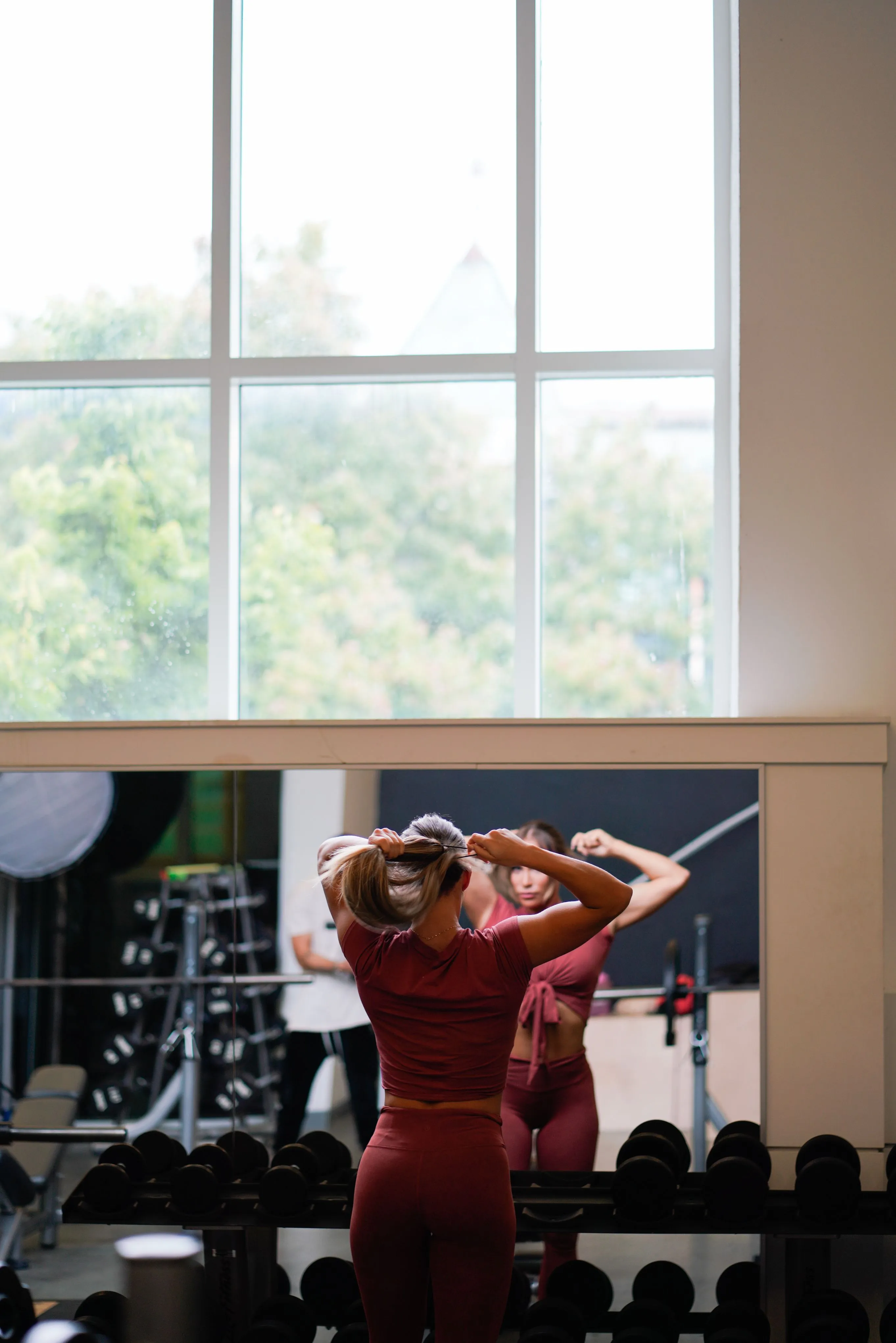 Girl putting on hair tie while staring in gym mirror